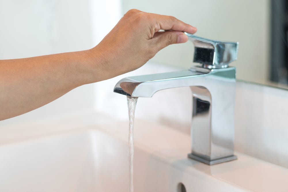 Hand pressing a faucet with running water.